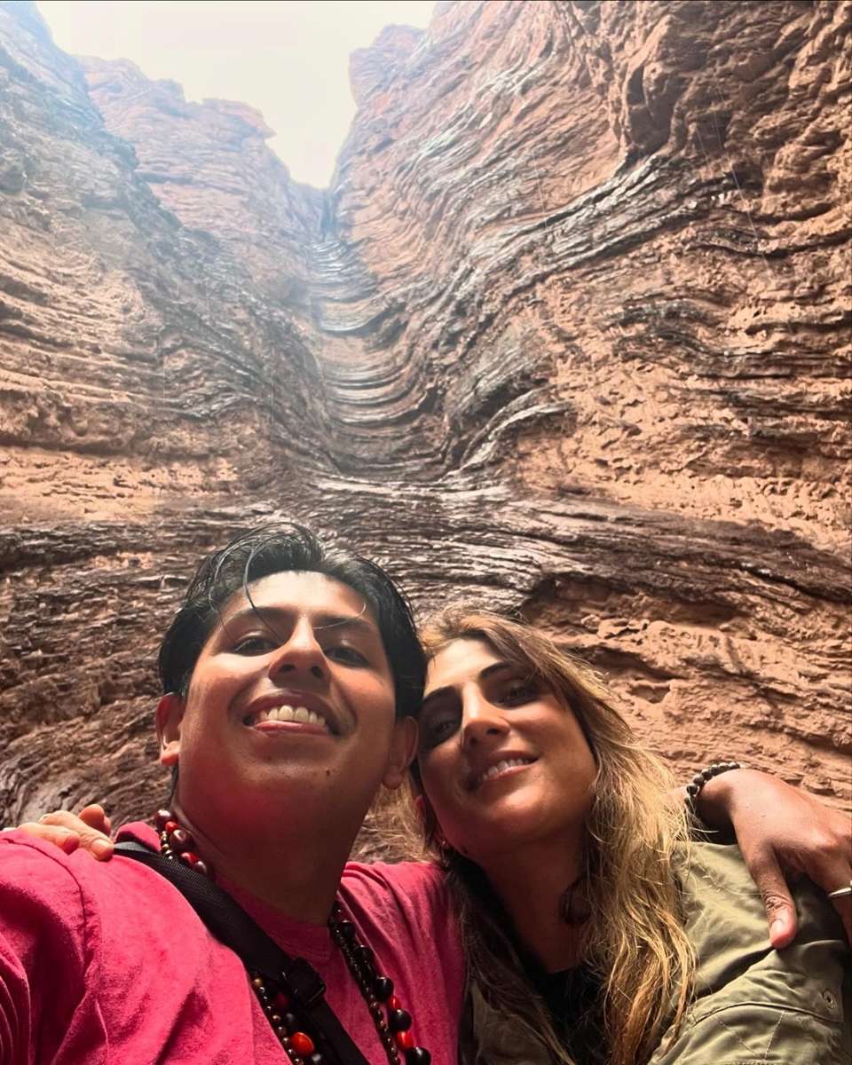 Dos personas abrazadas frente a una formación de roca en un cañón, de día, con el cielo despejado detrás.