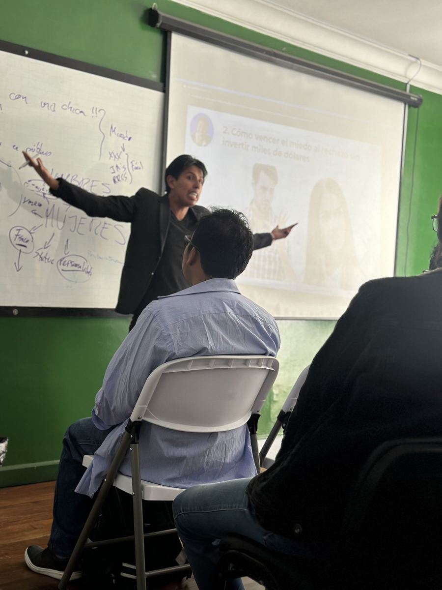 Pablo Montes de pie, con el brazo extendido señalando la pantalla, dando un taller a un grupo de hombres sentados de espaldas.