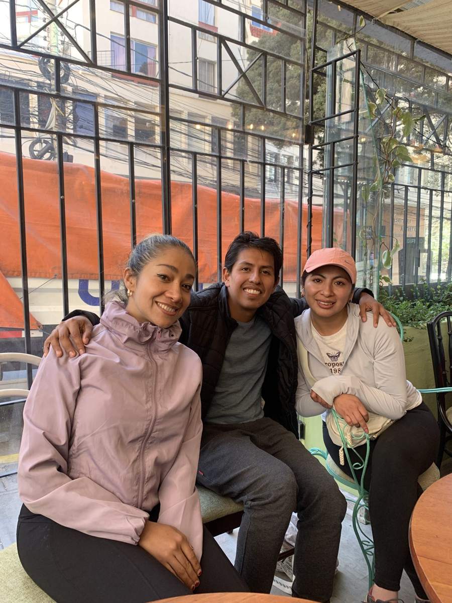 Tres personas en ropa deportiva sentadas en la terraza de un café de día, conversando.