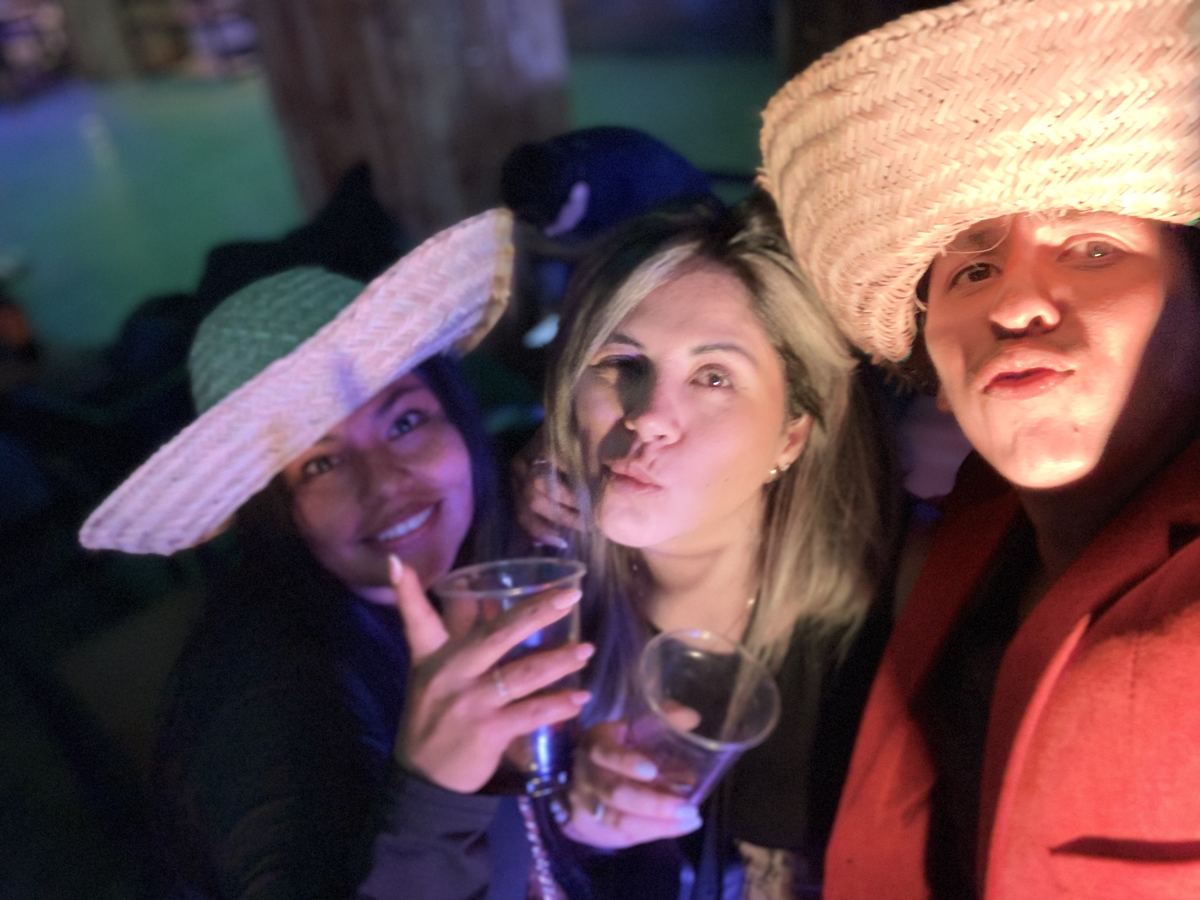 Tres personas con sombreros riéndose en una fiesta de noche.