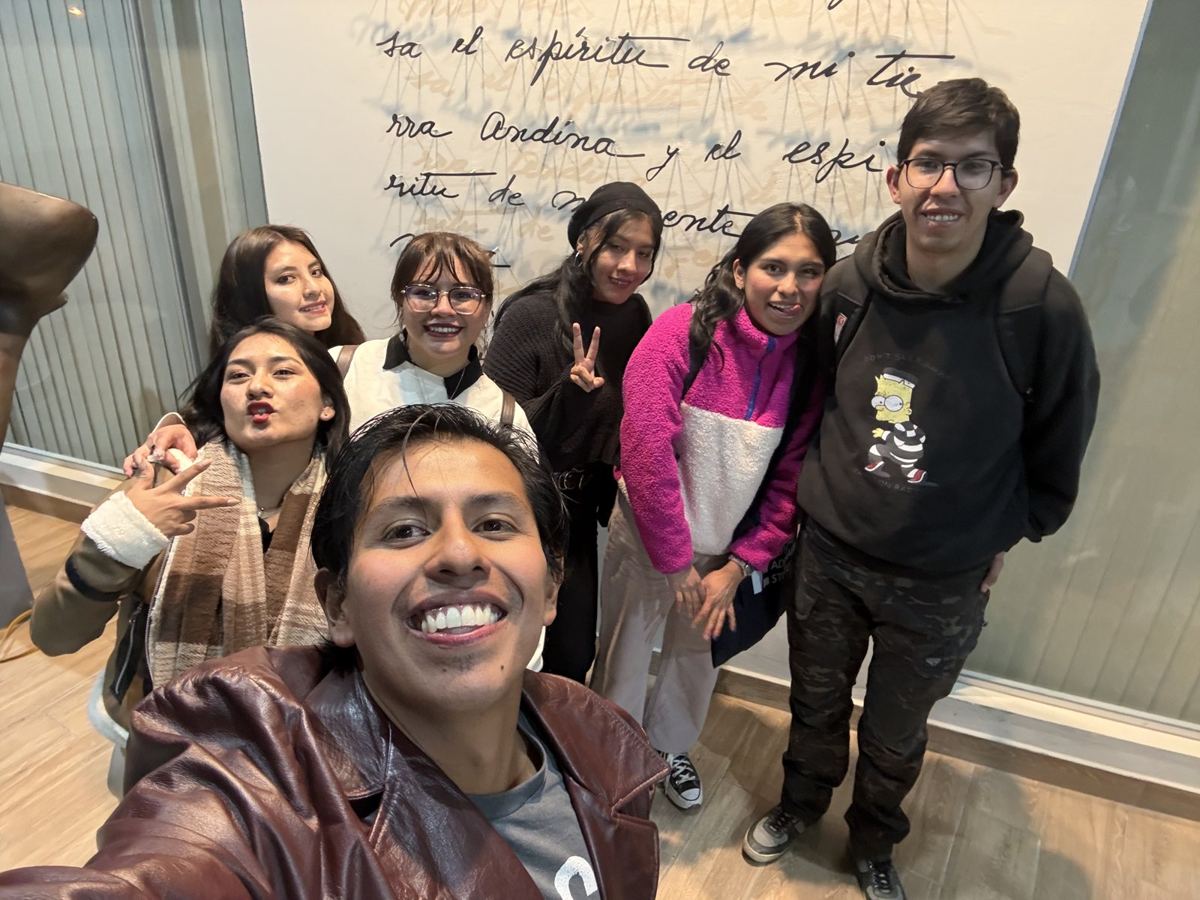 Grupo de siete personas jóvenes posando frente a una pared con un texto escrito a mano. Pablo Montes se toma la foto desde adelante.
