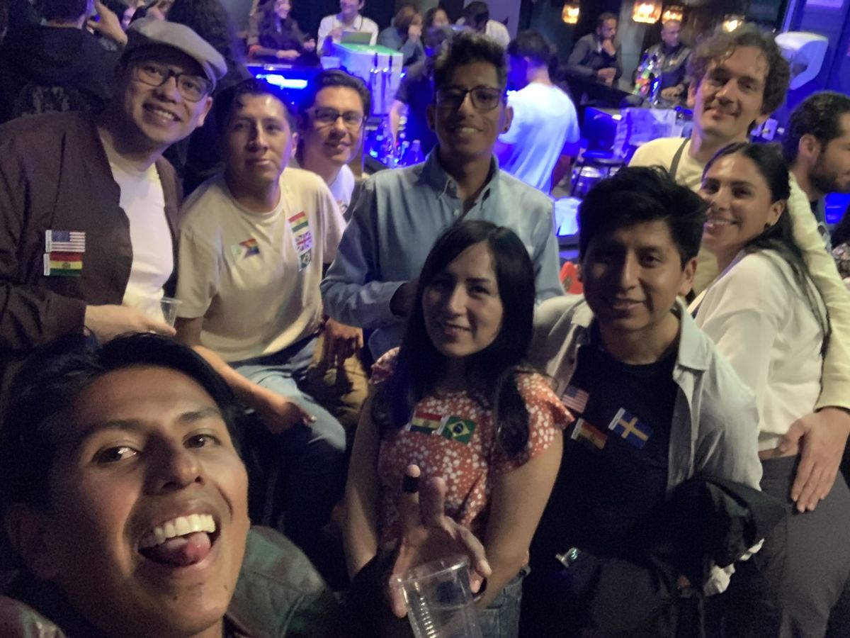 Grupo grande de personas sentadas alrededor de una mesa en un evento de intercambio de idiomas, con stickers de banderas de varios países pegados en la ropa.