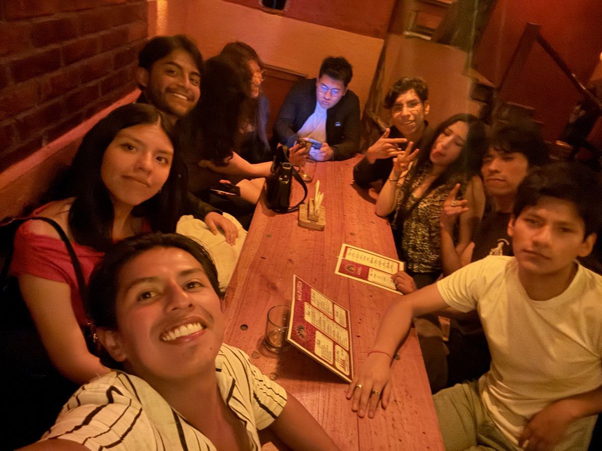 Nueve personas sentadas a los dos lados de una mesa larga de madera en un bar, con las cartas del menú sobre la mesa.