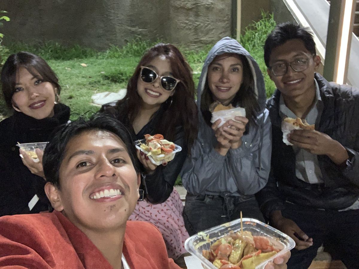 Cinco personas sentadas al aire libre comiendo comida callejera, de noche.